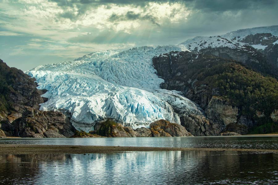 Glacier flowing between mountains into a still channel in Magallanes, Chile