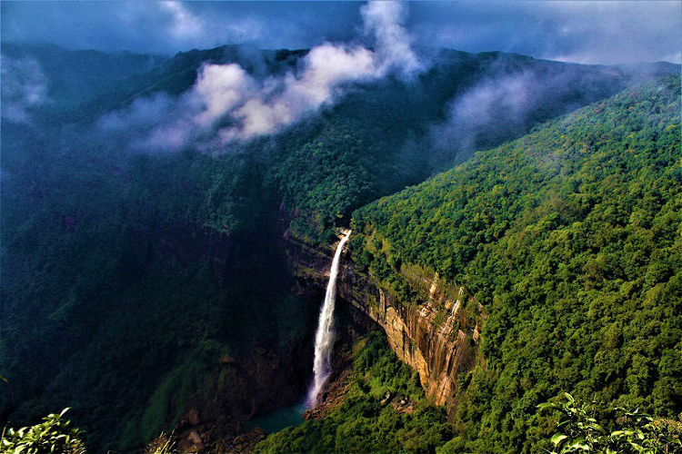 A waterfall dropping from forested cliffs beneath low cloud in Meghalaya, India